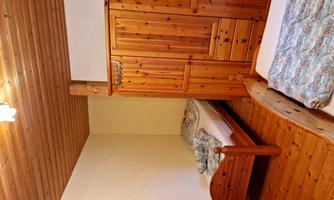 A simple bedroom with two single beds and a wooden wardrobe. The floor is wooden and the walls are lightly painted.