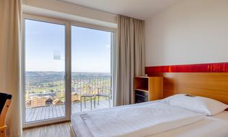 A modern hotel room with a double bed and large windows. The view of the countryside is clear and inviting.