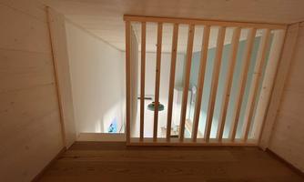 A view from a wooden staircase into an open space with a staircase and green wall decor. The wooden paneling gives the room warmth and coziness.