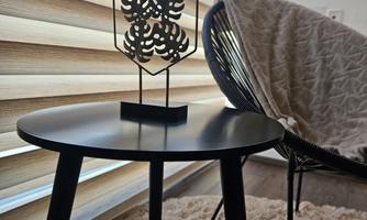A stylish table with a decorative object and a cozy chair. The room has large windows with striped curtains.