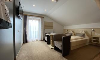 A modern room with two beds and a cozy sitting area. Large windows provide plenty of natural light.