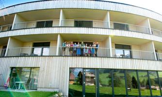 A modern residential complex with several balconies. A group of people is standing on the balcony and posing happily.