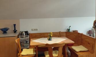 A cozy dining kitchen with a wooden bench and table. On the table is a vase with a flower.