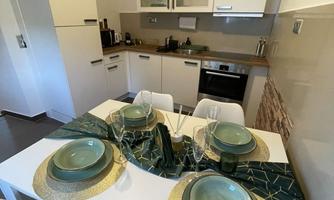 A modern kitchen with an elegant dining table that is set. The green and gold decoration creates an inviting atmosphere.