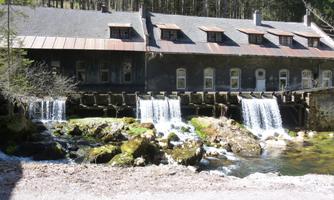 An old building next to a clear water stream and waterfalls. Surrounded by trees and nature.