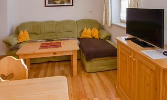 A cozy living room with a green couch and a wooden coffee table. A television is on a wooden furniture piece in the corner.