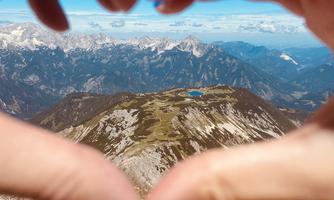 A heart made of hands in front of an impressive mountain landscape. In the background, snow-capped peaks and a clear blue sky can be seen.
