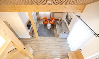A modern living room with a cozy sofa and two orange armchairs. The room has large windows and a bright, inviting look.