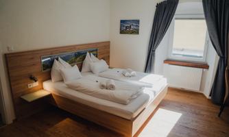 A cozy hotel room with a double bed, white bedding, and two pillows. Large windows let in plenty of natural light.
