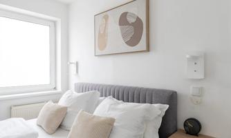 A modern bedroom with a large bed and soft pillows. A stylish piece of art hangs on the wall, and a bedside table stands next to the bed.