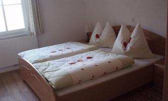 A cozy bedroom with a double bed and two pillows in tent shape. The decor is simple and bright.