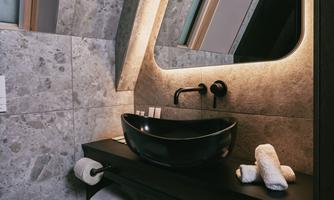 A modern bathroom with gray stone walls and elegant lighting. The black sink and white towels create a stylish look.