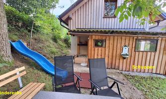 A cozy garden area with wooden furniture and a slide for children. In the background, there is a wooden shed and a recreational area.