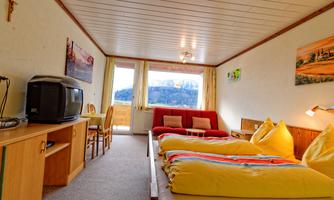 A cozy hotel room with two beds and a red sofa. Large windows offer a view of the countryside.