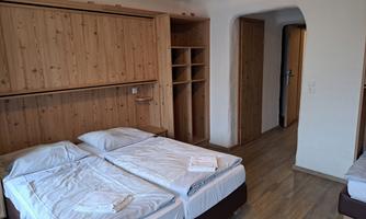 A simple bedroom with two beds and a wooden wardrobe. The room has a bright and functional character.