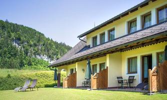 A modern guesthouse with a well-maintained garden. In the background, green hills and a clear sky can be seen.