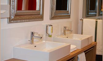 A modern bathroom with two sinks and elegant mirrors. The decor is stylish with wooden and white elements.