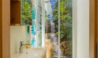 A modern bathroom with a shower and a sink. Behind the shower, there is a picture of a waterfall and trees, creating a natural atmosphere.