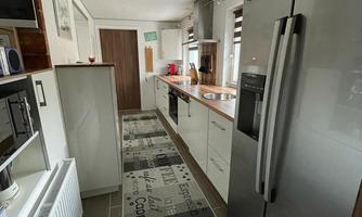 A modern kitchen with a refrigerator, a countertop, and a decorative rug mat. The space is bright and well-organized.
