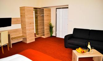A modern room with a black sofa, a table, and a small bar with fruit and drinks. The room features a wardrobe and a television.