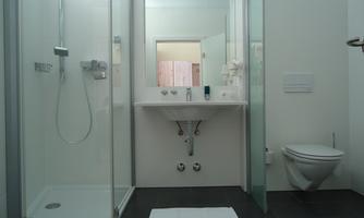 A modern bathroom with a shower, a sink, and a toilet. The room has bright walls and a minimalist style.