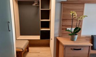 A modern wardrobe with open shelves and a seating area. Next to the wardrobe is a chest of drawers with a blooming plant.