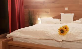 A cozy bedroom with a large bed and white pillows. A sunflower lies on the bedspread, and the walls are covered with wood.