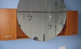 A modern bathroom with a round mirror and a white wash basin. The walls are light blue and wooden cabinets provide storage space.