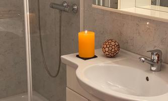 A modern bathroom with a shower and a sink. On the sink, there is an orange candle and a decorative ball.