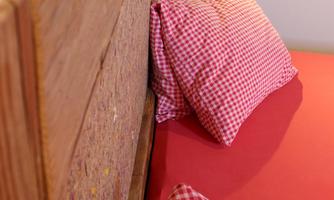 A warm bed with a rustic wooden headboard and checked pillows. The bedding is red and creates a cozy atmosphere.