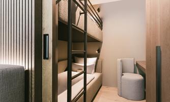 A modern bedroom with a bunk bed and a cozy seating area. The walls are in warm wood tones, creating an inviting atmosphere.