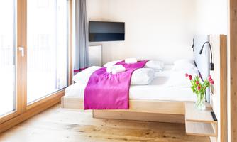 A modern bedroom with a large bed and colorful bedding. Plenty of daylight enters through the large windows.