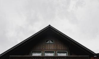 A view of the roof of a wood-clad house under a gray sky. The architecture features windows and a balcony.