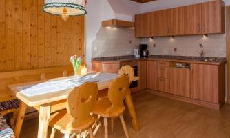 A cozy kitchen with wooden furniture and a dining table. The walls are bright and the floor is made of wood.