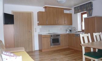 A modern kitchen with wooden cabinets and a dining table. The room is designed to be bright and welcoming.