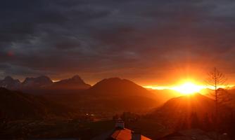A breathtaking sunset over the mountains with orange light. The sky is covered with dark clouds, making the scene look dramatic.