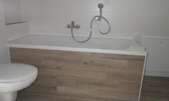 A bright bathroom with a modern bathtub and a shower. The walls are kept in neutral colors and the floor is tiled with wooden floor tiles.