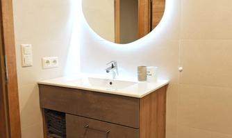 A modern bathroom with a wooden sink cabinet and a round mirror. The wall is designed to be bright and simple.