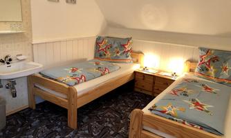 A cozy room with two beds and colorful bedding. There is a mirror above the sink, and there is a small bedside lamp.