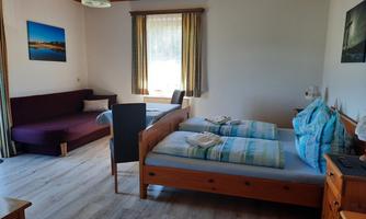 A cozy room with two beds and a sofa.  
Bright walls and wooden details create a pleasant atmosphere.