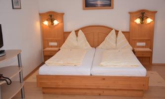 A cozy bedroom with a double bed and light wood details. The walls are in soft colors, and there are nightstands with lamps.