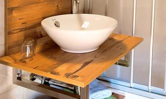 A modern bathroom with a ceramic sink and a wooden shelf. Towels in soft colors are neatly arranged.