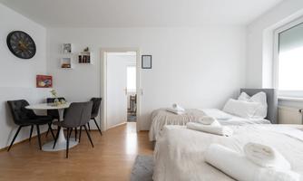 A bright, modern room with two single beds and a small dining area. The walls are in soft tones, and there are some decorative elements.