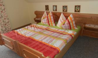 A cozy bedroom with a large wooden bed and colorful pillows. Small pictures hang on the wall, and the carpet is gray.