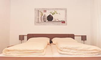 A modern bedroom with a large bed and bright bedding. On the wall hangs a decorative picture with vases and a plant.