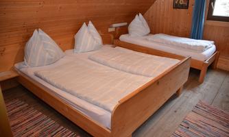 A cozy bedroom with two wooden bed frames. The walls are paneled with wood and there is a colorful carpet on the floor.