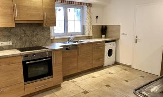 A modern kitchen with wooden cabinets and bright tiles. It has a sink, a stove, and a washing machine.