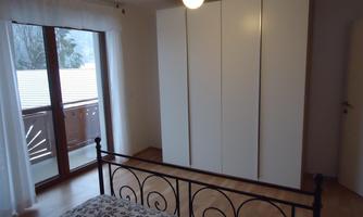 A cozy bedroom with an iron bed and a large white wardrobe. The room has plenty of daylight and large windows.