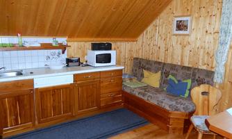 A cozy kitchen with wooden paneling and a small dining area. The room features a kitchenette, a microwave, and a couch with cushions.