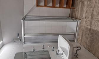 A modern bathroom with a shower cabin and a sink. There is also a wooden shelf next to the shower.